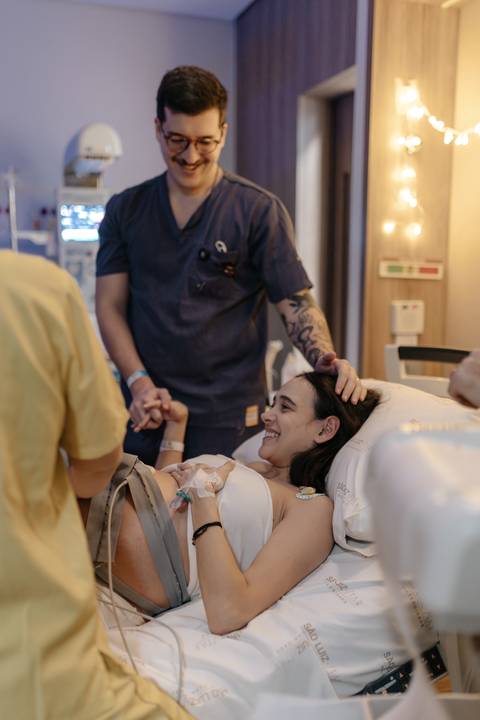 Acompanhante e equipe médica apoiando a gestante sorridente.'