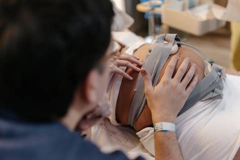 Acompanhante com a mão na barriga da gestante. '