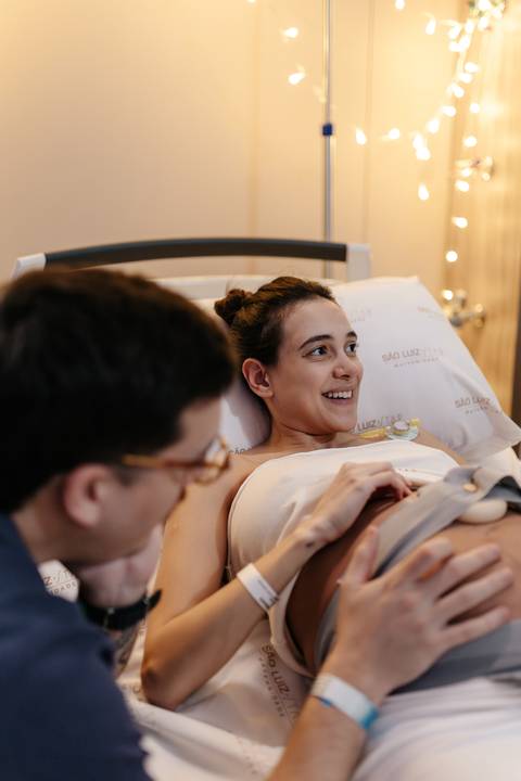 Gestante sorrindo para o acompanhante durante conversa na cama.'