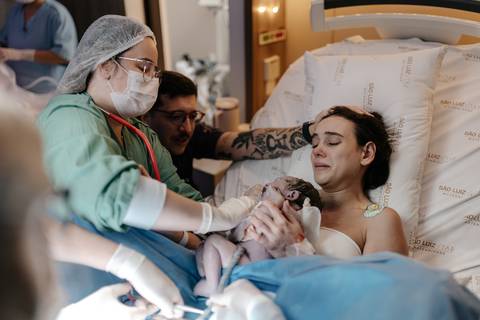 Bebê recém-nascido no colo da mãe recebendo o primeiro atendimento da médica.'