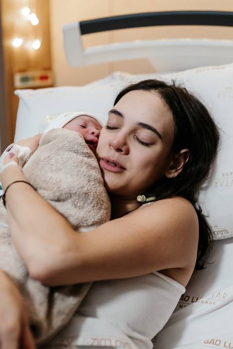 Mãe com o bebê nos braços com expressão de alívio e amor.'