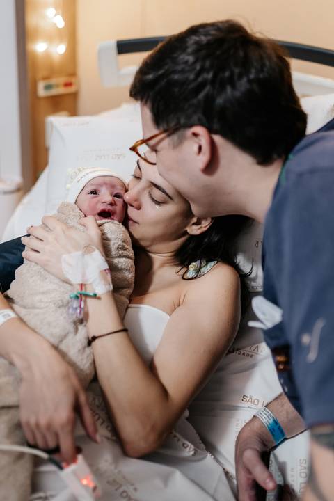 Família unida com o pai beijando a mãe enquanto ela segura a bebê.'