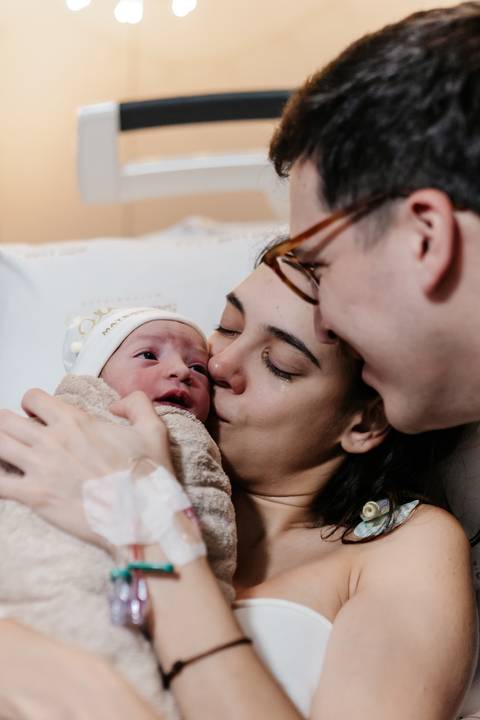 Mãe e pai beijando o bebê recém-nascido no colo.'