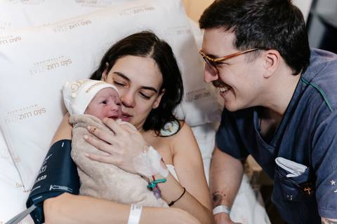 Casal sorrindo feliz com a bebê Olívia nos braços.'
