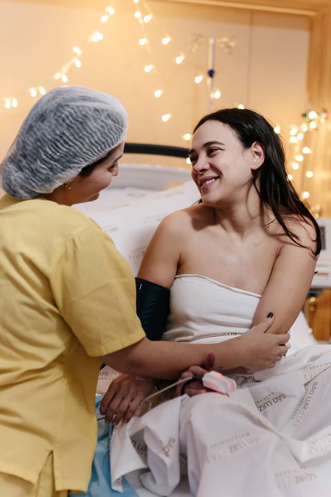 Profissional de saúde aferindo a pressão da mãe na cama.'