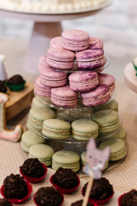 Torre de macarons cor-de-rosa e verde na mesa do bolo.'