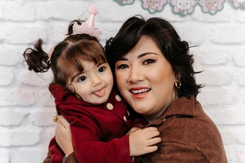 Mãe abraçada com a filha fazendo graça para a câmera.'