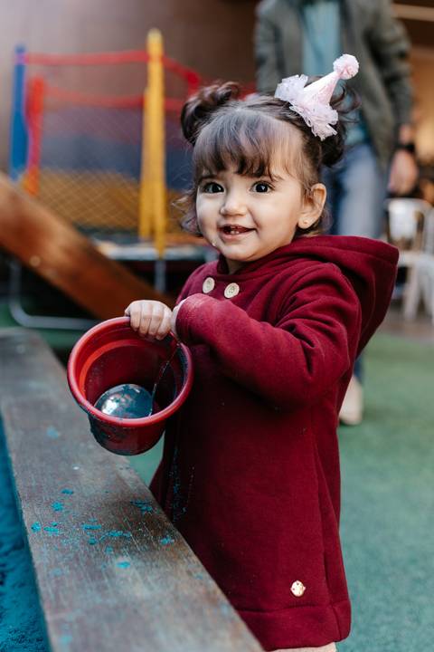 Menina brincando com um balde vermelho no espaço de brincar.'