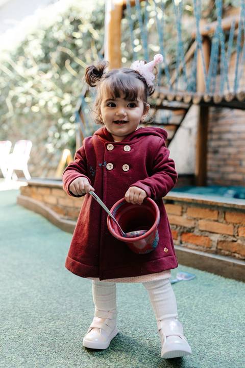 Menina segurando a alça do balde no parque infantil.'