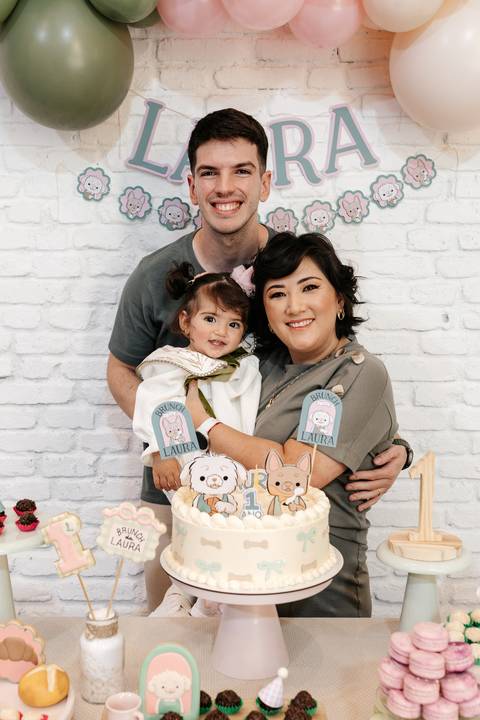 Mãe segurando a filha no colo atrás do bolo de aniversário.'
