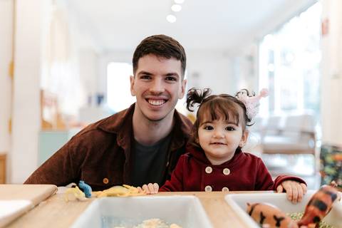 Pai e filha sorrindo juntos na mesa de atividades de brinquedo.'