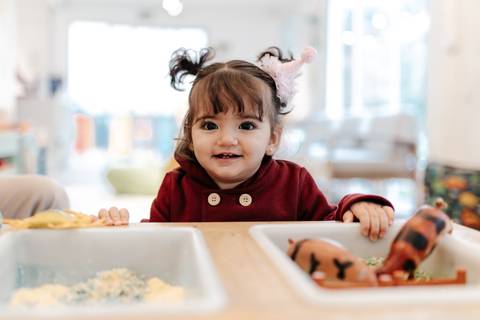 Menina sorridente brincando com dinossauros de brinquedo na mesa.'
