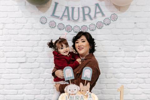 Mãe com a filha no colo sorrindo em frente ao painel decorativo.'