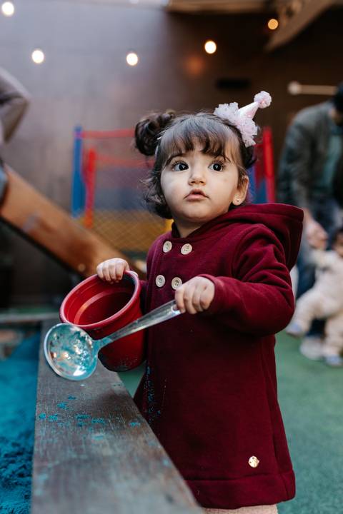 Menina com uma concha grande brincando no espaço de areia.'