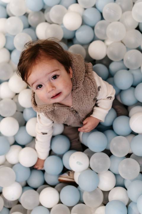 Bebê deitado e sorrindo no meio da piscina de bolinhas.'