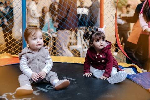 Duas crianças sentadas juntas no pula-pula do espaço infantil.'