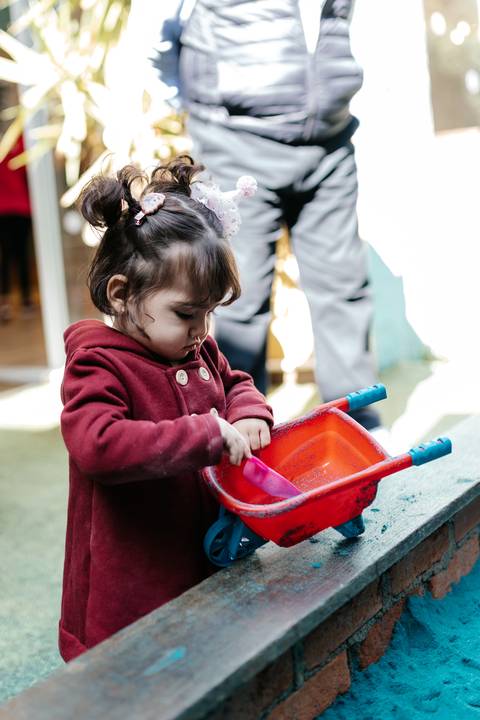Menina usando uma pá para encher a bacia de brinquedo na areia.'