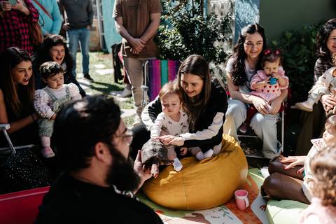 Convidados reunidos em círculo no chão participando da recreação infantil.'
