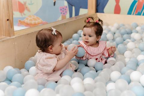 Duas bebês brincando juntas dentro da piscina de bolinhas.'