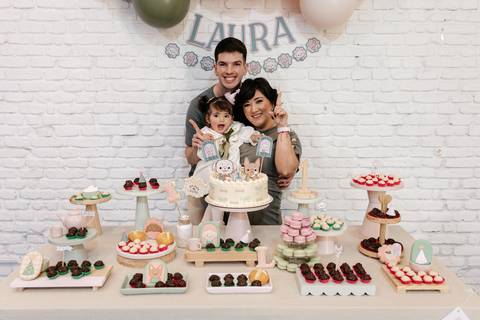 Família unida e sorridente atrás da mesa de doces decorada.'