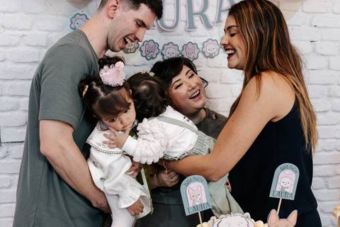 Família e convidada abraçadas e sorrindo juntas no momento do parabéns.'