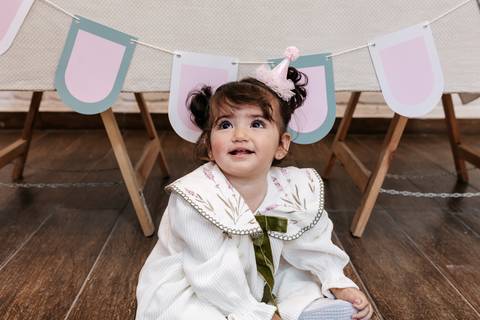 Aniversariante de vestido branco com laço verde sorrindo no chão.'