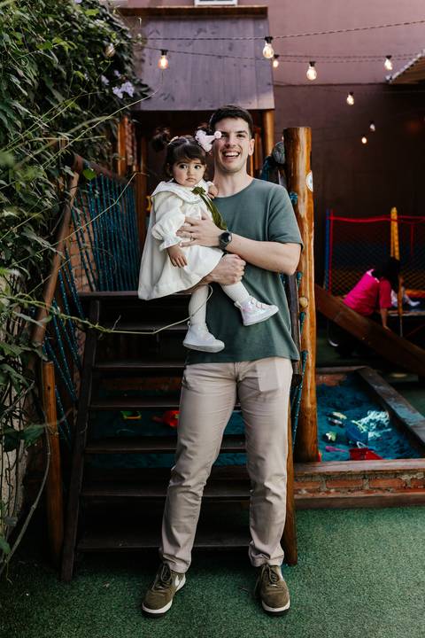 Pai segurando a filha no colo no parque infantil de madeira.'