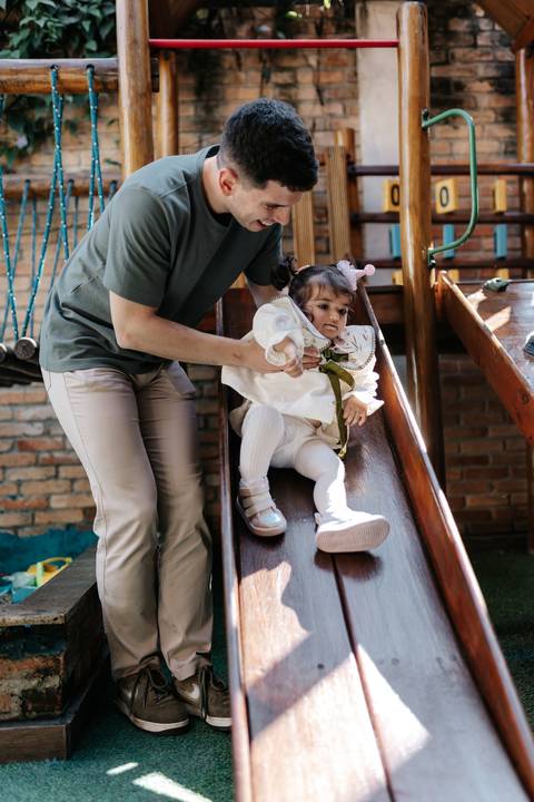 Pai ajudando a filha a descer no escorregador do parquinho.'