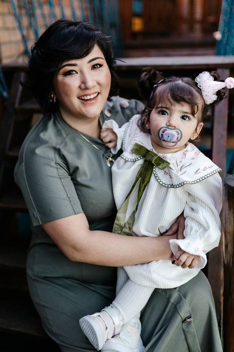 Mãe segurando a filha de chupeta no colo sorrindo.'