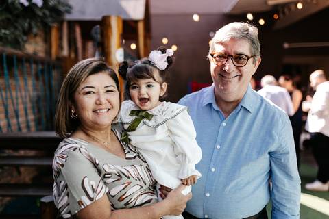 Avós sorridentes segurando a neta no colo no espaço externo.'