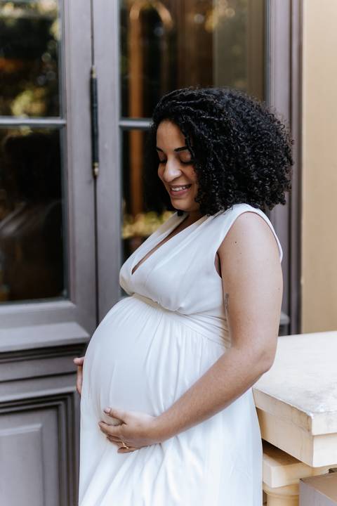 Gestante de vestido branco olhando carinhosamente para a barriga.'