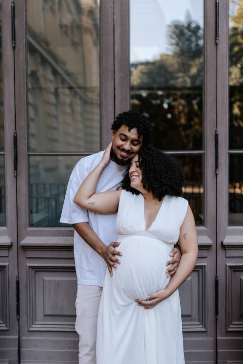 Casal sorridente abraçado em frente à janela histórica.'