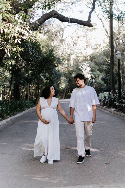 Casal passeando de mãos dadas na alameda arborizada.'