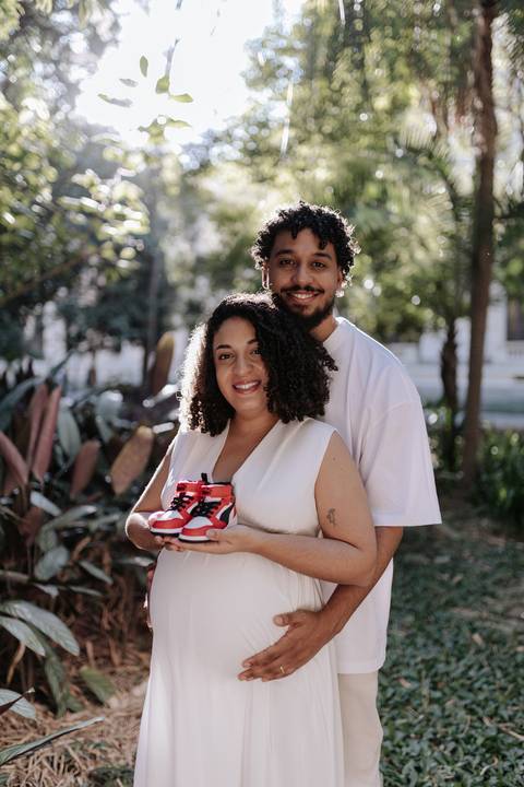 Casal sorrindo segurando um par de tênis infantis vermelhos.'