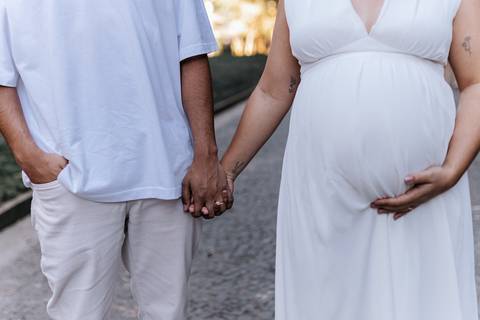 Plano detalhe do casal de mãos dadas exibindo o vestido e a barriga.'