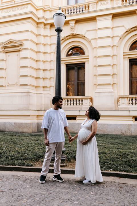Casal de mãos dadas sorrindo em frente à fachada do museu histórico.'