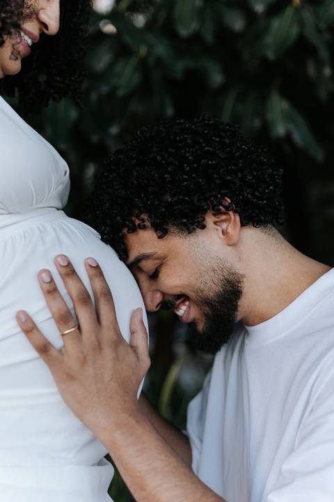 ai sorrindo com o rosto encostado carinhosamente na barriga da gestante.'