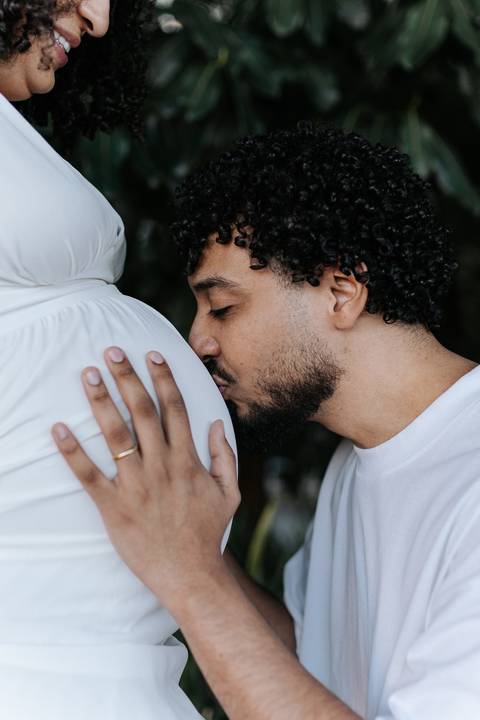 Pai dando um beijo afetuoso na barriga da gestante em detalhe aproximado.'