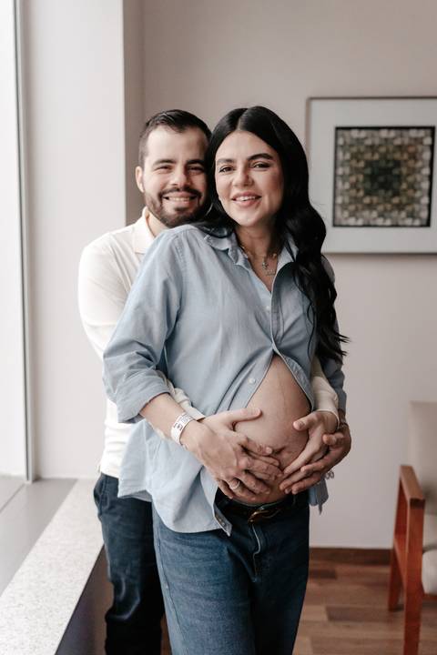 Pai abraçando a gestante por trás e segurando sua barriga.'