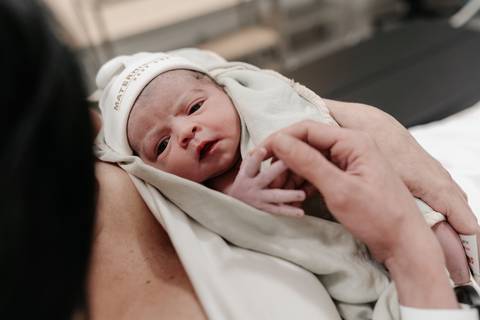 Bebê recém-nascido olhando curioso no colo da mãe.'
