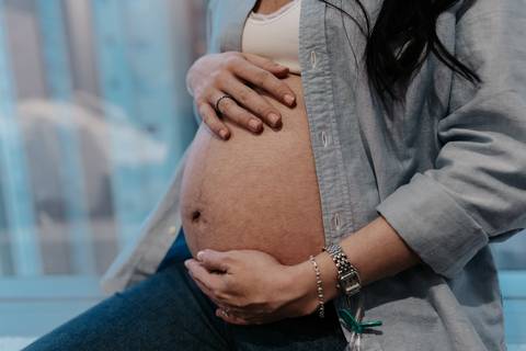 Close-up da barriga de grávida com camisa jeans sobreposta.'