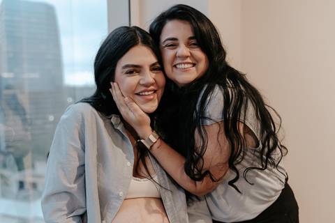 Duas mulheres sorrindo abraçadas e celebrando a chegada do bebê.'