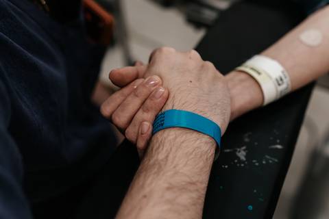 Mãos do casal firmemente unidas com pulseira de identificação hospitalar.'