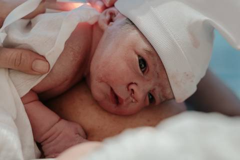 Recém-nascido de touquinha olhando atentamente para a mãe no peito.'