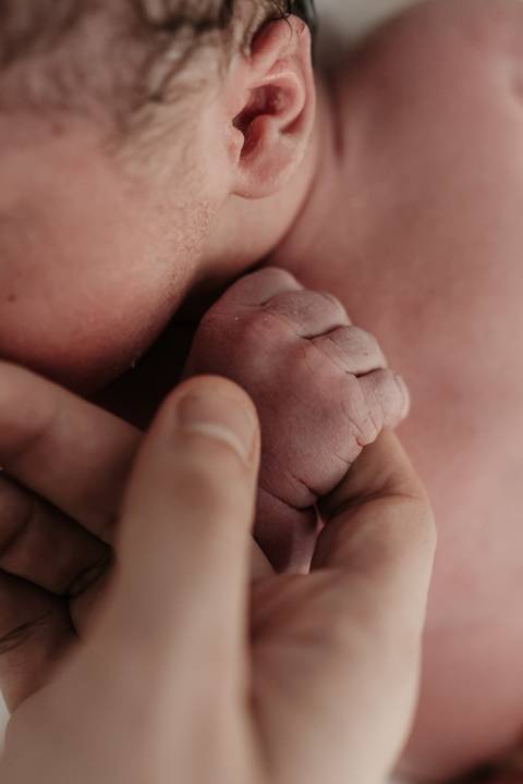 Macro da mãozinha do bebê segurando o dedo de um dos pais.'