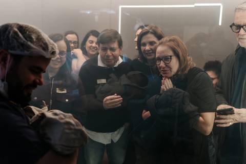 Família emocionada reunida em frente ao painel de vidro assistindo ao nascimento.'