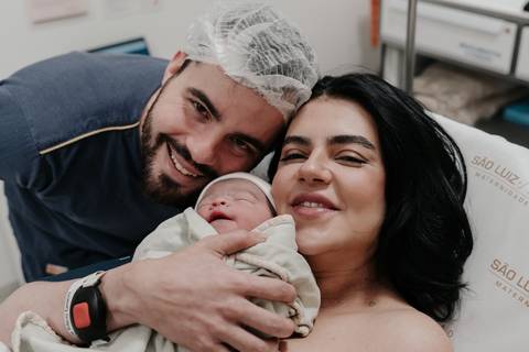 Retrato em família do casal sorrindo felizes com o bebê nos braços.'
