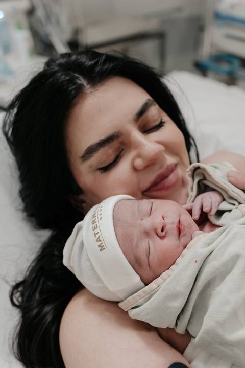 Mãe sorrindo de olhos fechados encostando o rosto no bebê.'