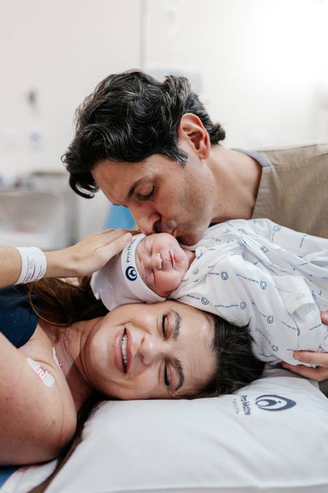 Pai beijando a cabeça da mãe e do bebê em retrato de família emocionado.'