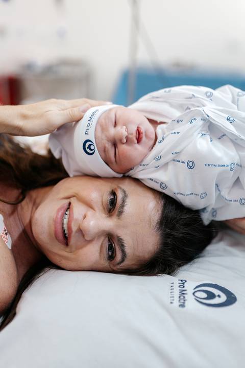 Retrato do casal sorrindo com o recém-nascido de touquinha da Pro Matre.'